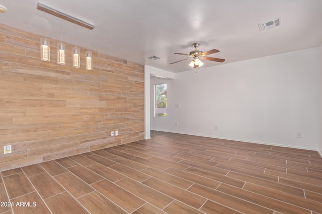 empty room featuring ceiling fan, hardwood / wood-style floors, and wood walls