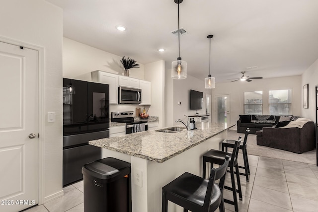 kitchen with sink, an island with sink, pendant lighting, stainless steel appliances, and white cabinets