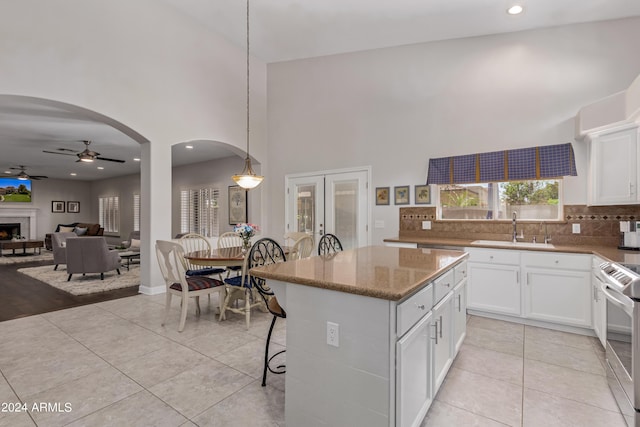 kitchen with stainless steel range oven, sink, white cabinetry, a center island, and hanging light fixtures