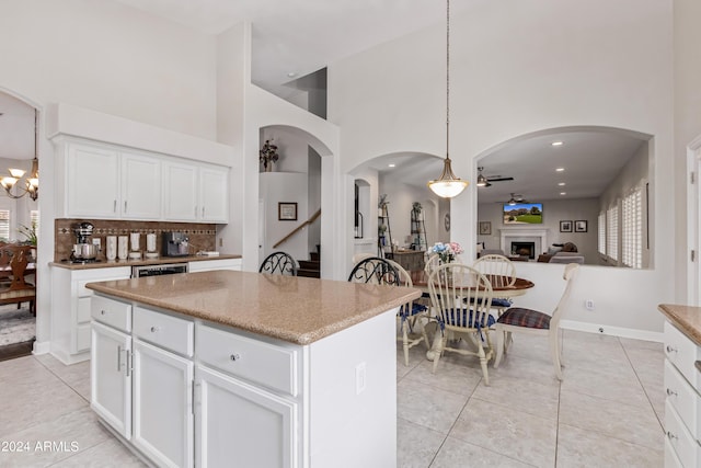 kitchen featuring light tile patterned flooring, a kitchen island, ceiling fan with notable chandelier, white cabinetry, and hanging light fixtures