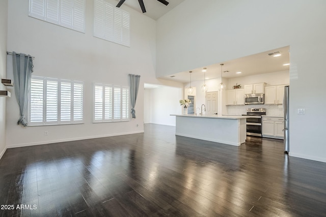 10925 E Toluca Ave, Mesa, AZ 85212 - unfurnished living room with a ceiling fan, a towering ceiling, dark wood-style flooring, a sink, and baseboards