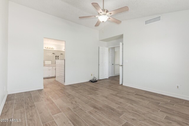 3805 E Desert Flower Ln, Phoenix, AZ 85044 - unfurnished bedroom featuring light wood-style flooring, lofted ceiling, baseboards, ensuite bath, and a textured ceiling