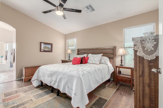 bedroom with ensuite bathroom, vaulted ceiling, ceiling fan, hardwood / wood-style flooring, and multiple windows