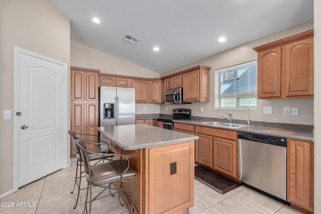 kitchen with vaulted ceiling, appliances with stainless steel finishes, a kitchen bar, a kitchen island, and sink