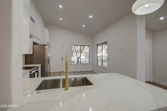 kitchen with light stone countertops, stainless steel range, sink, lofted ceiling, and light wood-type flooring