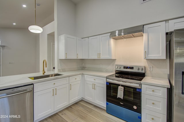 kitchen featuring sink, wall chimney range hood, decorative light fixtures, white cabinets, and appliances with stainless steel finishes