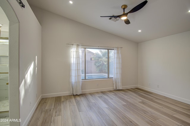 spare room with a barn door, ceiling fan, vaulted ceiling, and light wood-type flooring