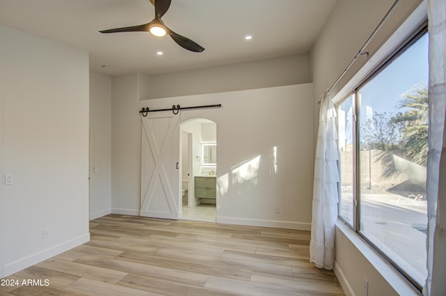 spare room with light wood-type flooring, a barn door, and ceiling fan