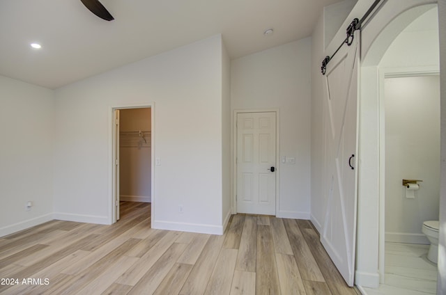 unfurnished bedroom with light wood-type flooring, ensuite bath, a barn door, a spacious closet, and a closet