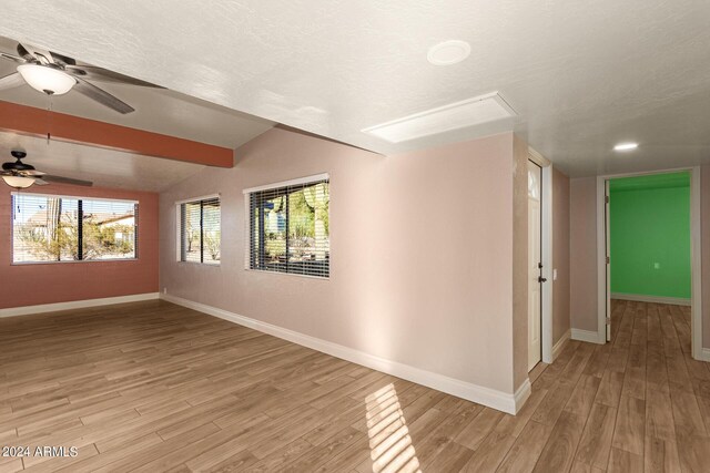 spare room featuring lofted ceiling with beams, light hardwood / wood-style floors, ceiling fan, and a textured ceiling