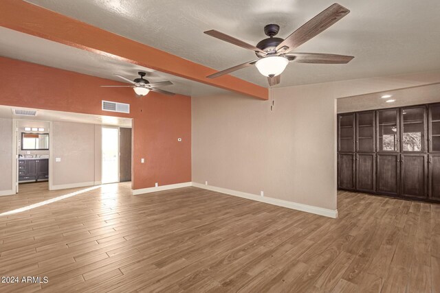 unfurnished living room with ceiling fan, a textured ceiling, beam ceiling, and wood-type flooring