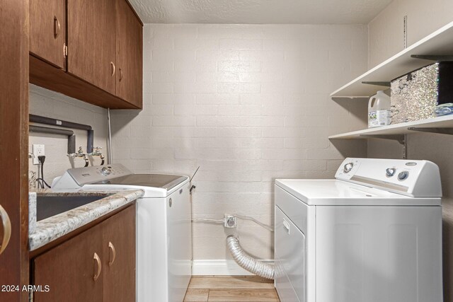 laundry room featuring independent washer and dryer, brick wall, a textured ceiling, light hardwood / wood-style flooring, and cabinets