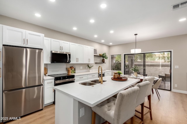 kitchen with visible vents, an island with sink, a sink, stainless steel appliances, and white cabinetry