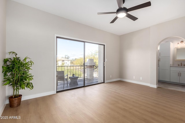 spare room featuring arched walkways, light wood finished floors, baseboards, and a ceiling fan