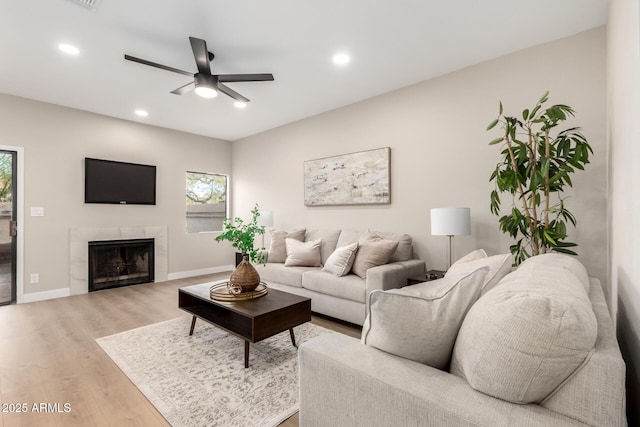 living area with baseboards, ceiling fan, light wood-type flooring, recessed lighting, and a tile fireplace