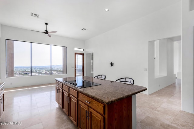 kitchen featuring a kitchen island, visible vents, black electric cooktop, and dark stone counters