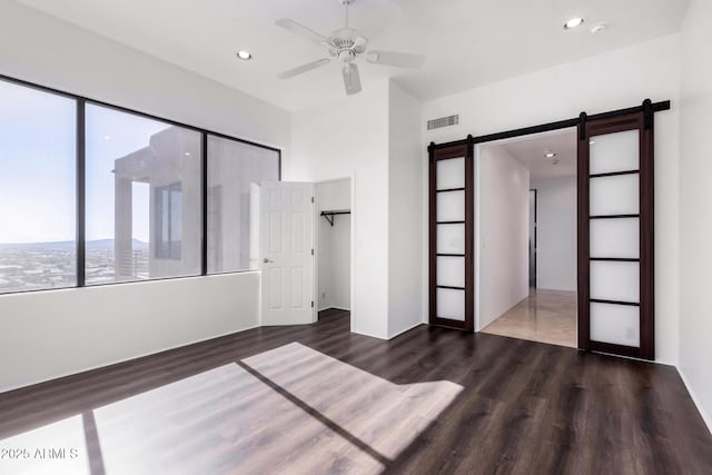 unfurnished bedroom with a barn door, visible vents, wood finished floors, a closet, and recessed lighting