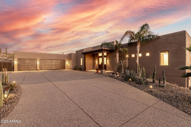 adobe home featuring a garage, concrete driveway, and stucco siding