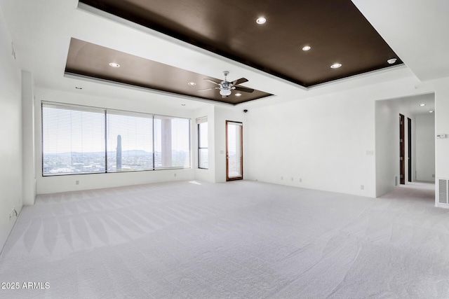 empty room with a ceiling fan, a tray ceiling, light colored carpet, and visible vents