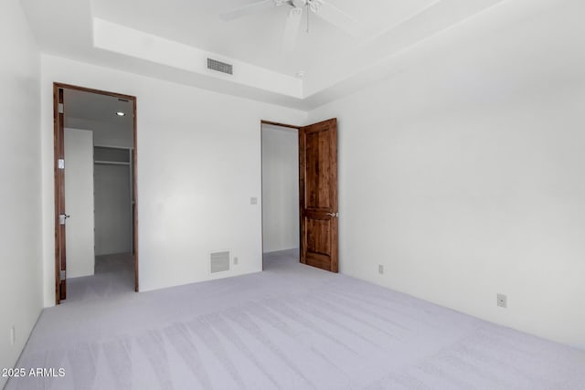 unfurnished bedroom featuring a spacious closet, visible vents, a tray ceiling, and carpet flooring