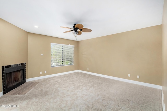 unfurnished living room featuring a ceiling fan, baseboards, carpet flooring, and a tile fireplace