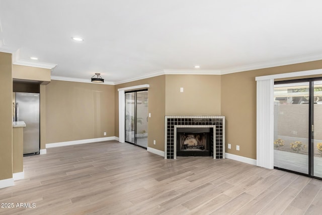 unfurnished living room with ornamental molding, light wood-type flooring, baseboards, and a tiled fireplace