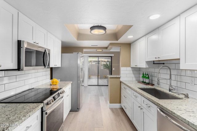 kitchen with white cabinetry, a tray ceiling, appliances with stainless steel finishes, and a sink