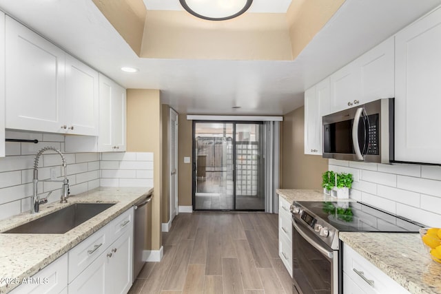 kitchen with a sink, white cabinetry, light wood-style floors, appliances with stainless steel finishes, and a tray ceiling