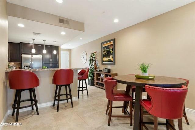 kitchen featuring kitchen peninsula, hanging light fixtures, light stone countertops, stainless steel fridge with ice dispenser, and a breakfast bar