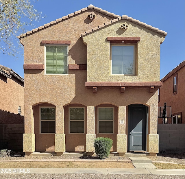 view of front facade featuring a tiled roof, stucco siding, and fence