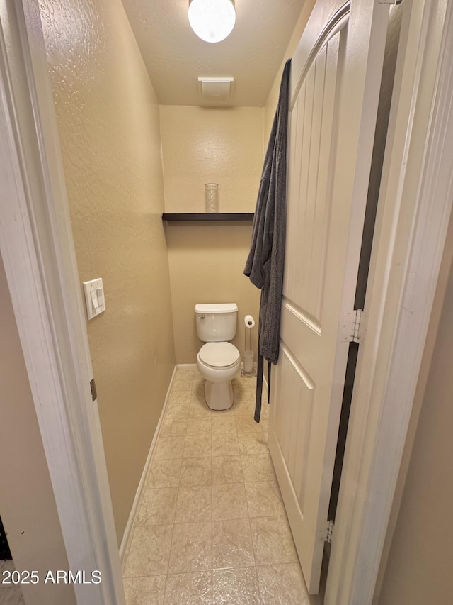 bathroom featuring baseboards, toilet, tile patterned flooring, and a textured wall