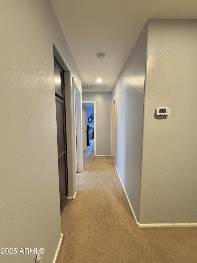 hall with light carpet, visible vents, baseboards, and a textured wall