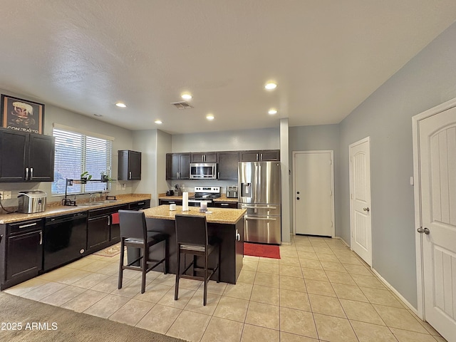 kitchen featuring visible vents, an island with sink, light tile patterned floors, a kitchen breakfast bar, and stainless steel appliances