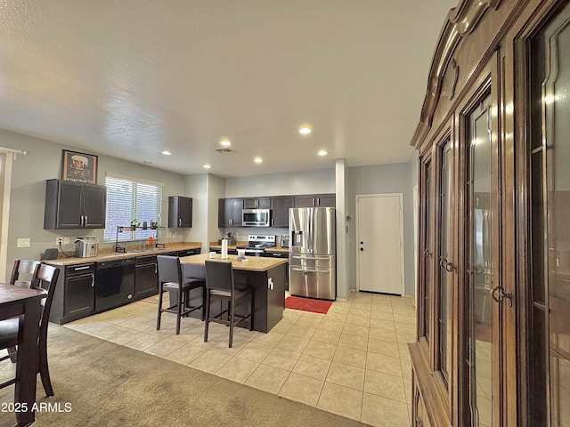 kitchen featuring a center island with sink, a kitchen bar, recessed lighting, appliances with stainless steel finishes, and light tile patterned flooring