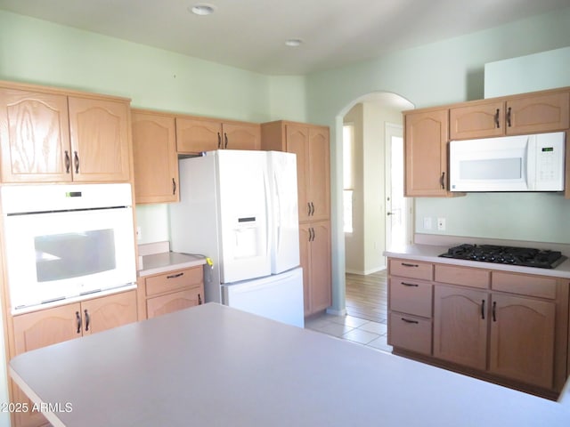 kitchen with light brown cabinets, white appliances, and light tile patterned floors