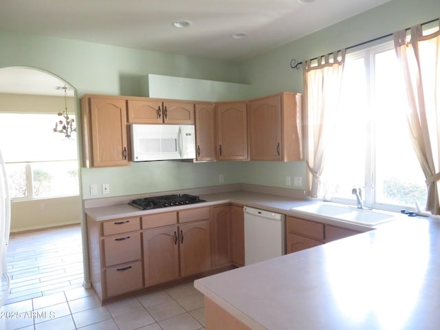 kitchen with sink, white appliances, light tile patterned floors, hanging light fixtures, and light brown cabinets