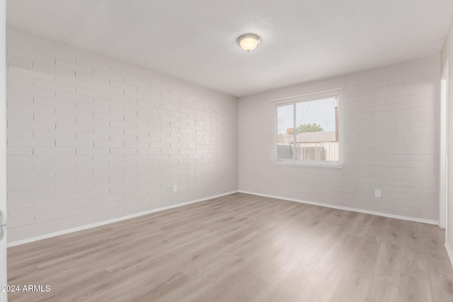 spare room with light hardwood / wood-style floors and brick wall