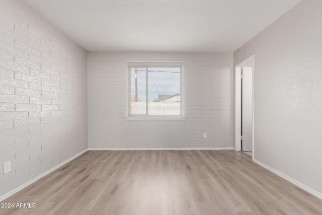 unfurnished room featuring light wood-type flooring and brick wall