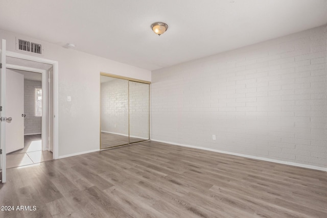 unfurnished bedroom with a closet, wood-type flooring, and brick wall