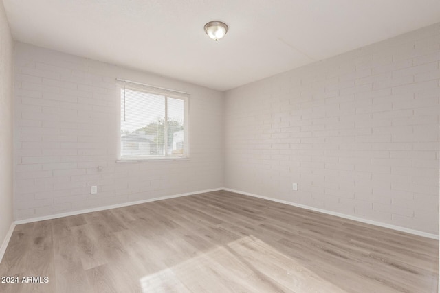 empty room with brick wall and light wood-type flooring