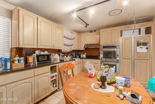 kitchen with dark stone countertops, a textured ceiling, rail lighting, light tile patterned floors, and stainless steel appliances