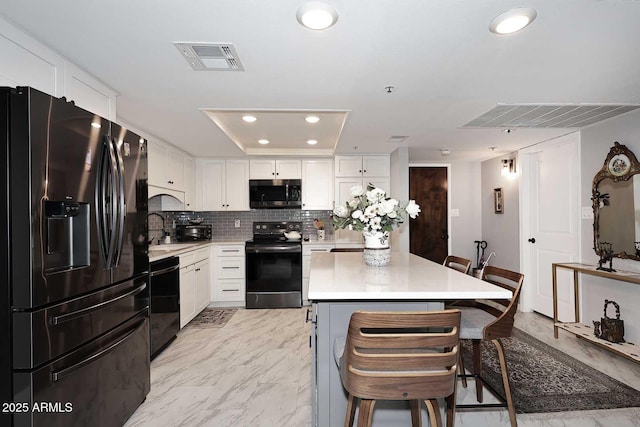 kitchen featuring a breakfast bar, visible vents, light countertops, black appliances, and recessed lighting
