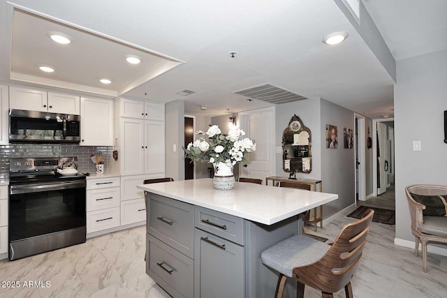 kitchen with recessed lighting, a kitchen bar, marble finish floor, light countertops, and appliances with stainless steel finishes