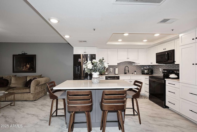 kitchen with black appliances, marble finish floor, a sink, and a tray ceiling