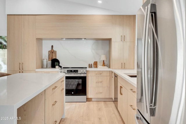 kitchen featuring lofted ceiling, appliances with stainless steel finishes, light brown cabinetry, and light wood-type flooring