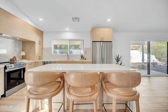 kitchen featuring sink, stainless steel appliances, a kitchen breakfast bar, a center island, and decorative backsplash