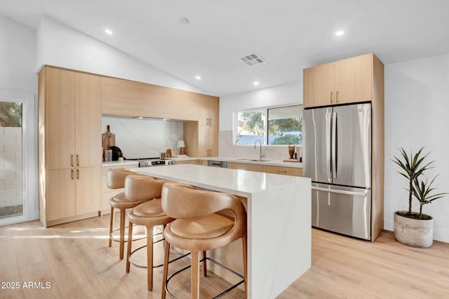 kitchen with sink, vaulted ceiling, stainless steel fridge, a kitchen island, and decorative backsplash