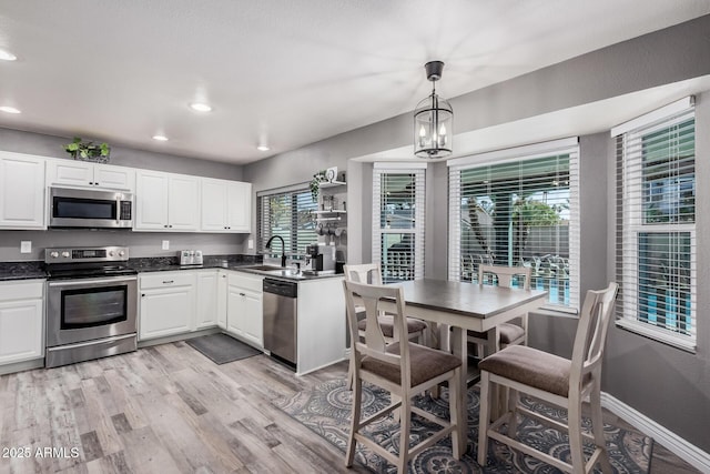 kitchen featuring dark countertops, light wood finished floors, stainless steel appliances, white cabinetry, and a sink