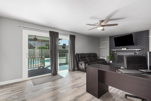 office featuring a brick fireplace, wood finished floors, baseboards, and ceiling fan