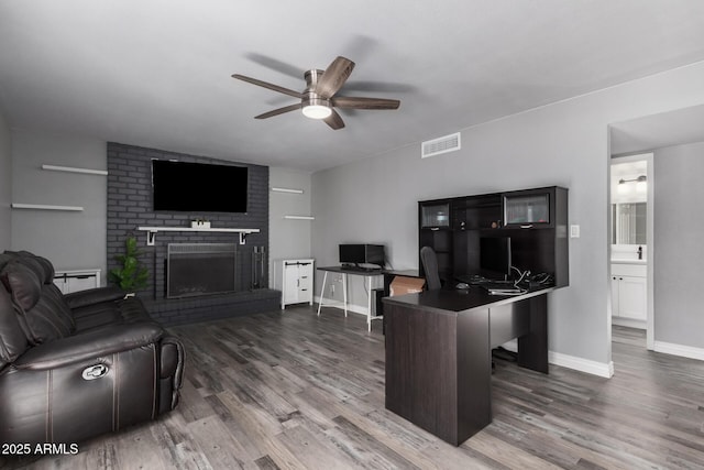 living area with visible vents, a fireplace, wood finished floors, and a ceiling fan